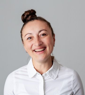 A photo of Matapo's business development manager, Elisabeth Ortelt. She has a hair bun, brown hair, and brown eyes, and is smiling broadly while wearing a white collared shirt against a neutral background.