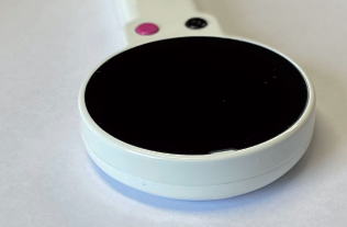 Front view of the Looky Round handheld magnifier, showing its circular screen and two control buttons, one pink and one black.