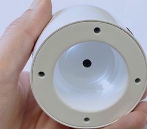 Bottom view of the Looky Round V2 magnifier held in a hand, showing the circular lens and built-in lighting surrounded by four small screws.