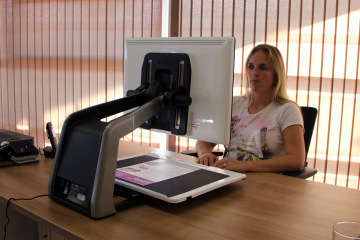 A woman sitting at a desk using the Acuity Speech desktop magnifier, with a large screen displaying enlarged text.