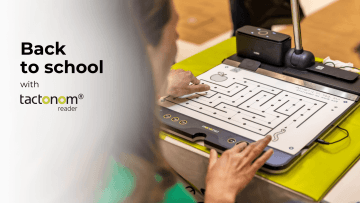 A person is interacting with a tactile reading device called tactonom reader. The image shows the person's hand tracing a maze on a tactile graphic displayed on the device. The background features a soft focus, highlighting the person’s engagement with the device. The text "Back to school with tactonom reader is prominently displayed on the left side of the image, blending seamlessly with the overall design. The scene suggests an educational setting, emphasizing the use of the device for accessible learning.